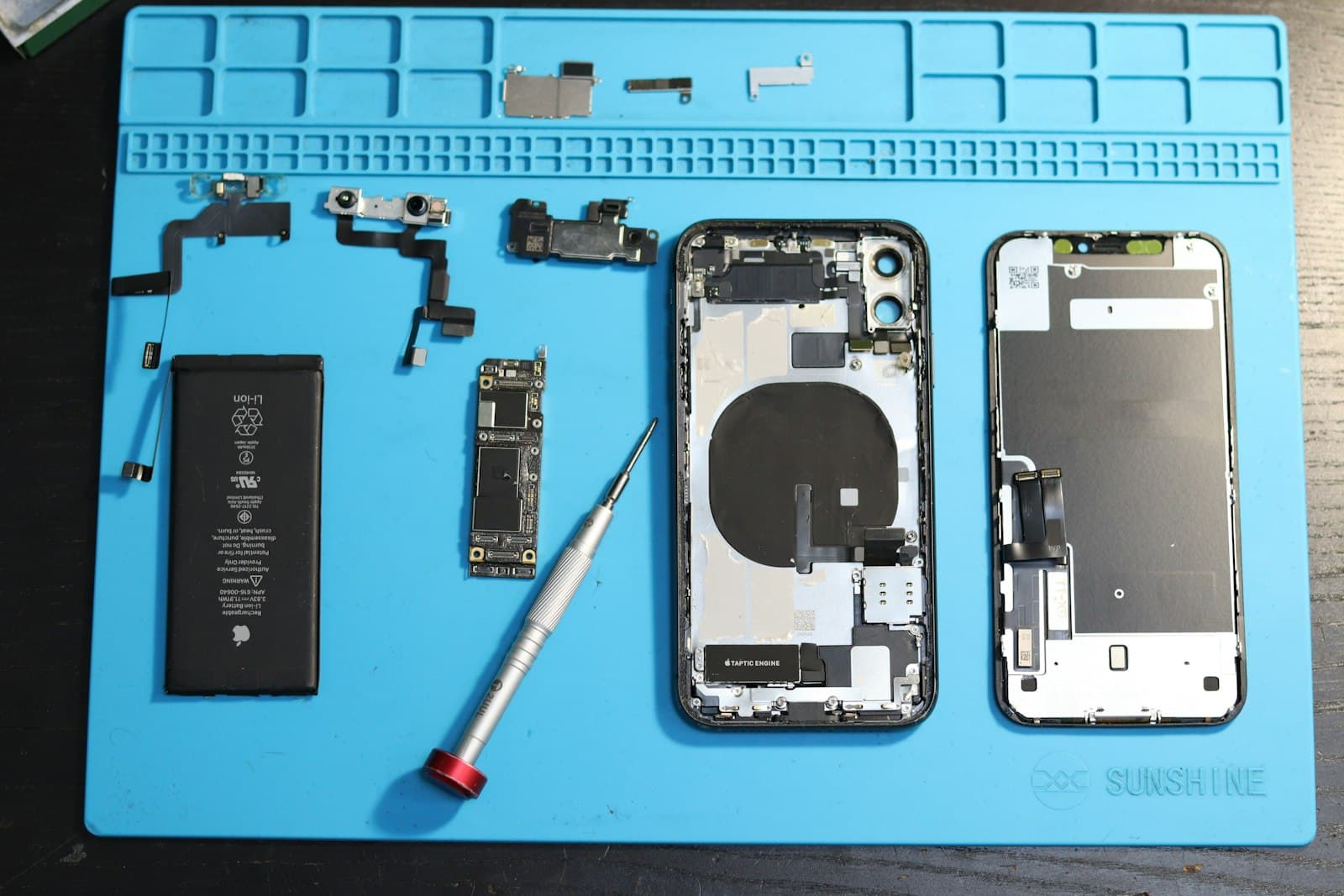 Komponen iPhone yang dibongkar tersusun rapi di atas alas kerja biru