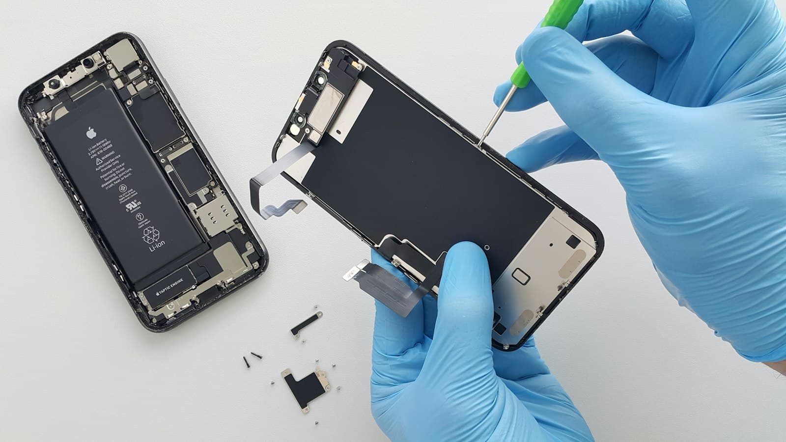 Teknisi bersarung tangan melepas layar iPhone dengan obeng