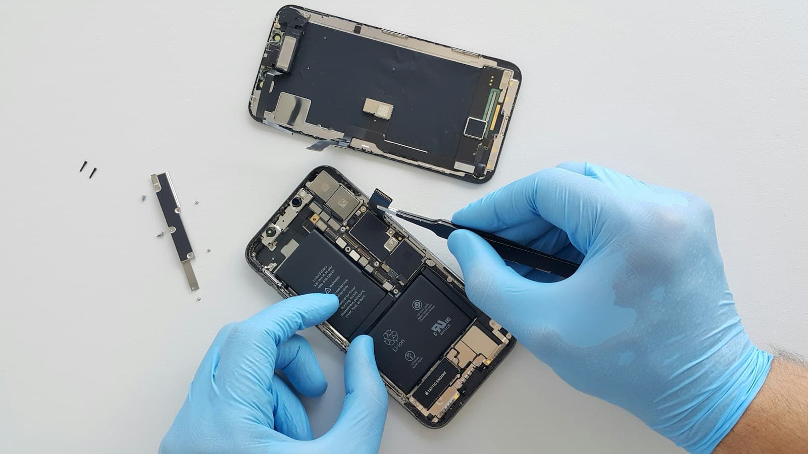 Teknisi bersarung tangan mengerjakan bagian dalam iPhone dengan pinset